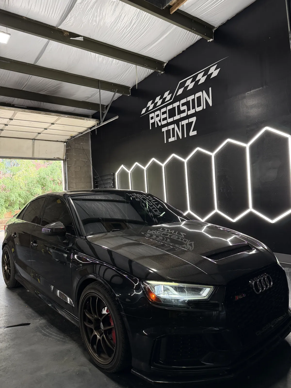 Glossy black Audi under the Precision Tintz hex lights showing the deep finish ceramic coating is designed to protect