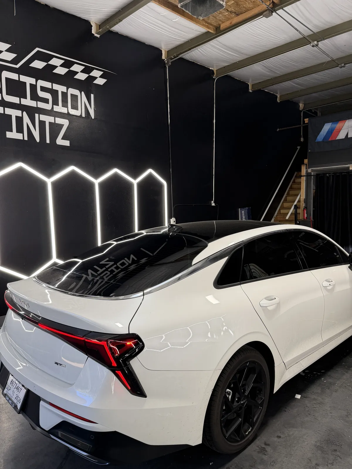 White Kia K5 sedan with fresh carbon window tint inside the Precision Tintz install bay in Aurora